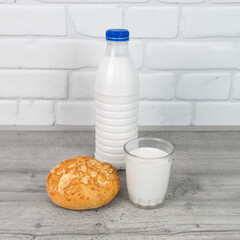bottle and a glass of milk with a bun on the kitchen table