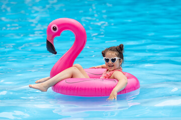 Happy little child girl swimming with flamingo pink inflatable ring in clean pool water while...