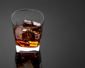 whiskey with ice in a transparent glass on a black background with highlights