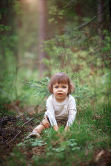 The toddler is sitting and playing in the forest, enjoying a carefree childhood. The child is running around in the green grass, living a summer lifestyle.