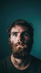Obraz premium A man with a beard gazes upwards against a teal background