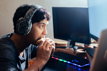 Young man eating sandwich while using computer