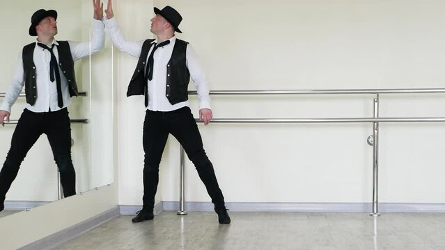 Reflection of a dancer in the mirror, a jazzman rehearses against the backdrop of a mirror in the hall. Blues dance of a man in a hat