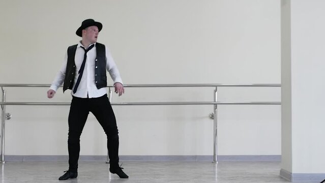 802 Gangster dance in a hat, jazzman dances by snapping his fingers, wearing a tie and vest. Creative dance of a young guy. Portrait of a man in a tie in rhythmic movement