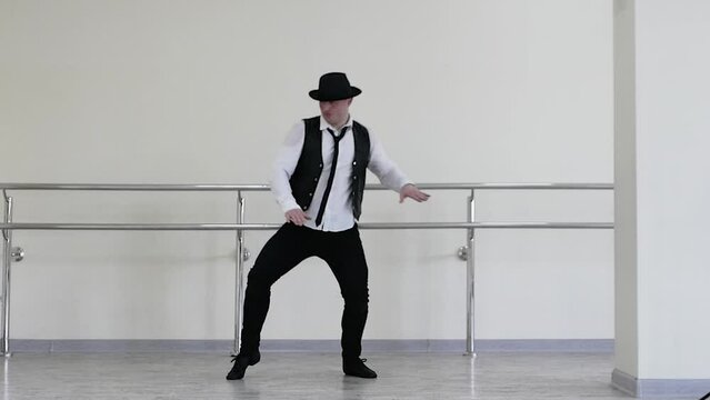 802 Gangster dance in a hat, jazzman dances by snapping his fingers, wearing a tie and vest. Creative dance of a young guy. Portrait of a man in a tie in rhythmic movement