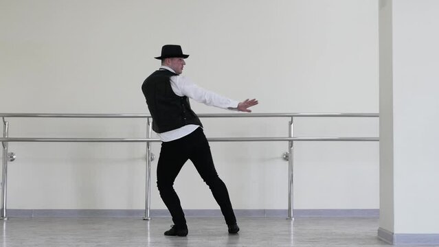 A gangster dances in a hat, a jazzman dances in a tie and vest. Creative dance of a young guy. Portrait of a man in a tie in rhythmic movement