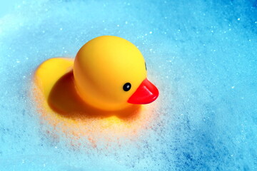 A rubber duck floats in the foam in the bathtub.