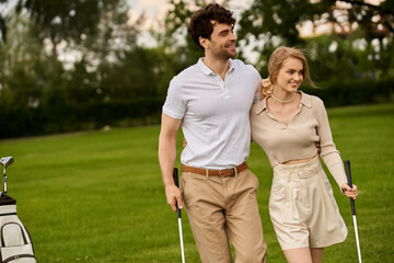 A young couple, elegantly dressed, walk on a golf course, enjoying each others company amidst lush...