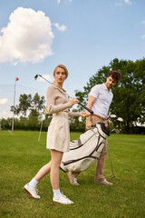 A stylish man and woman in elegant attire enjoy a leisurely walk on a luxurious golf course, surrounded by lush greenery.