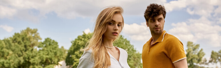 Beautiful young couple in elegant attire standing together on a green field, exuding luxurious old...