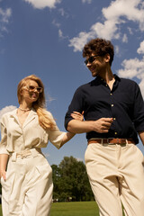 Fototapeta premium Elegant couple with old money style enjoying a leisurely walk through a vast green field under the sky.