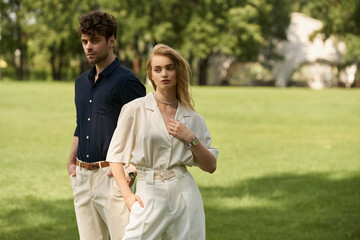 Fototapeta premium A stylish man and woman in elegant attire in a lush green park, exuding a sense of luxury and romance.