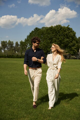 Fototapeta premium A graceful couple leisurely walks through a lush, grassy field, embodying a sense of peace and connection with nature.