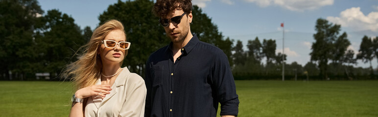 A man and woman in sunglasses, wearing elegant clothing, stand in a lush green field, exuding old-money style and a luxurious lifestyle.