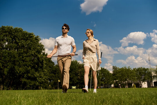 A stylish young couple in elegant attire strolls through a lush green grassy field in a golf club setting.