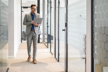 Male software developer smiling and doing online research over laptop while walking in office...