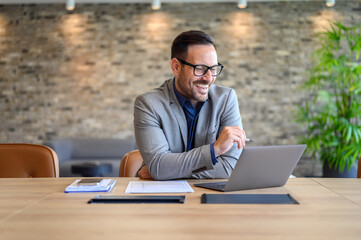 Portrait of cheerful male project manager planning over laptop during online meeting at desk in...