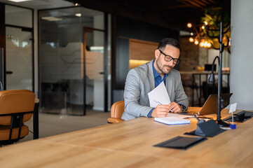 Young male manager in eyeglasses auditing financial report on desk at his workplace in modern office