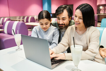 A happy family of four sits at a table, engaged with a laptop screen, spending quality time together in a modern setting.