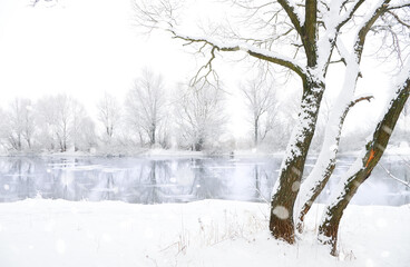 Heavy snowfall against the backdrop of a winter river and snow-covered trees.