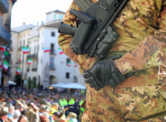 Army soldier in camouflage uniform with black gloves and assault rifle monitoring crowd in city...