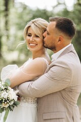 A bride and groom walk hand in hand through a pine forest, sunlight filtering through the trees, highlighting their joyful expressions.