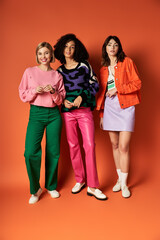 Fototapeta premium Multicultural women in stylish clothes stand united, showcasing friendship and diversity on an orange background.