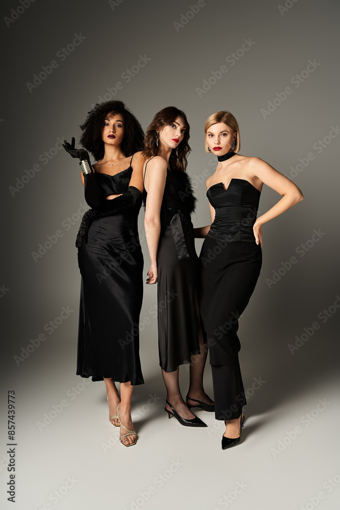 Poster Three stunning, diverse women in black dresses pose confidently against a grey backdrop.