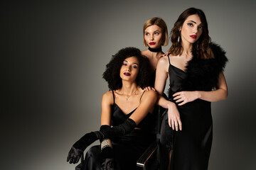 Three beautiful young women in black dresses posing gracefully for a stylish portrait on a grey backdrop.