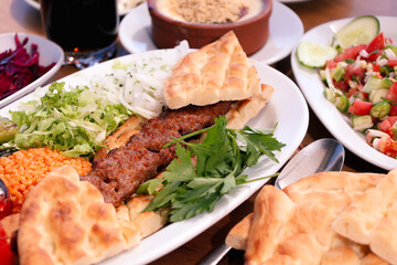 Grilled kebab served with bread, salad, and vegetables on a white plate, representing a hearty and satisfying meal.