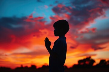 A young boy is seen praying towards the setting sun, conveying a sense of devotion and hope