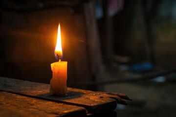 A lone candle burns brightly on a wooden surface, casting a warm glow in an otherwise dark room