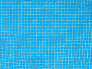 Outdoor swimming pool full of clear water with small square blue ceramic glossy mosaic tiles,...