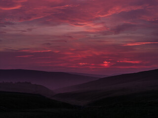 A breathtakingly vibrant sunset paints the sky in shades of pink and purple over rolling hills and misty valleys