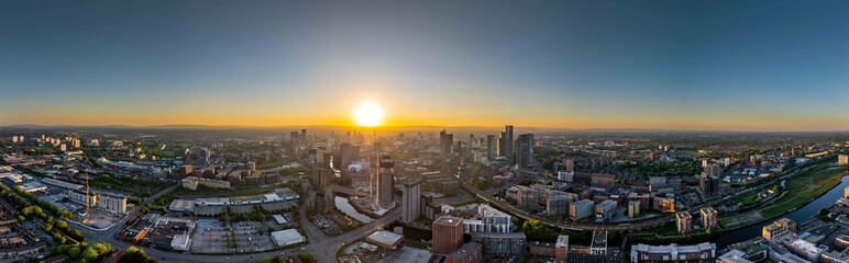 Fototapeta premium Featuring a wide cityscape of Manchester during sunset, the image foregrounds key areas like Deansgate and Salford Quays, as well as the The Great Jackson Street district