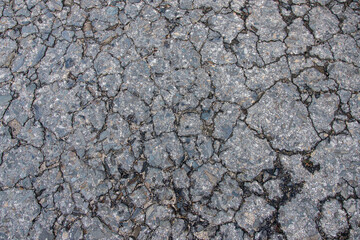 Close-up of a cracked asphalt surface, showcasing detailed texture and wear. The image captures the rugged and aged appearance of the pavement, highlighting natural deterioration over time.
