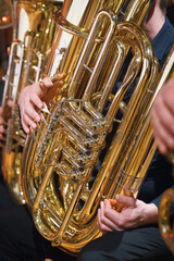 Hände, die eine glänzende Messingtuba spielen, Nahaufnahme der Finger des Musikers und der...
