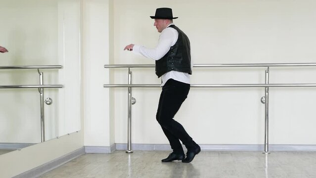 Rhythmic dance cha cha or bachata. Handsome young dancer in creative jazz clothes. Street Dancer in a hat with a tie and a black vest and jazz shoes, against the background of a wall.