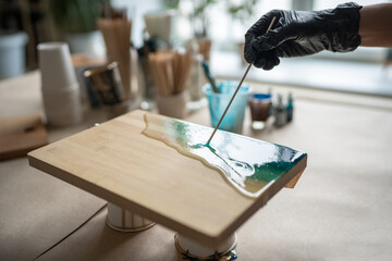Hand of female artist with wooden stick creating pattern of liquid, epoxy resin mixed with blue...