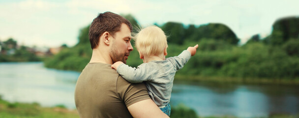 Caucasian father holding his son, dad and child walking together in summer park