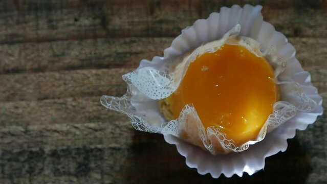 A close-up shot and a slow zoom in on an egg custard on the table (Quindim candy). Rays of sunlight randomly moving over an egg dessert. A top view of an egg yolk custard. A Brazilian coconut custard 