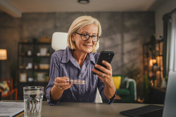 Mature woman hold the medicine and read instructions on mobile phone