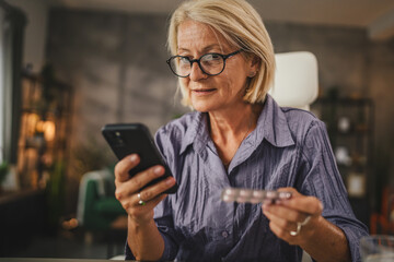 Mature woman hold the medicine and read instructions on mobile phone