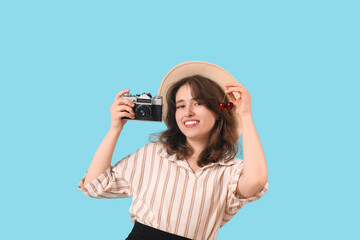 Beautiful woman in wicker hat with camera and ripe cherries on blue background