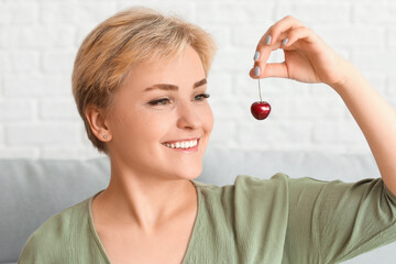 Beautiful happy young woman with ripe cherries in living room
