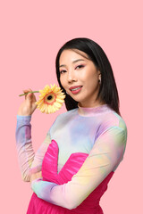 Happy young Asian woman with yellow gerbera flower on pink background