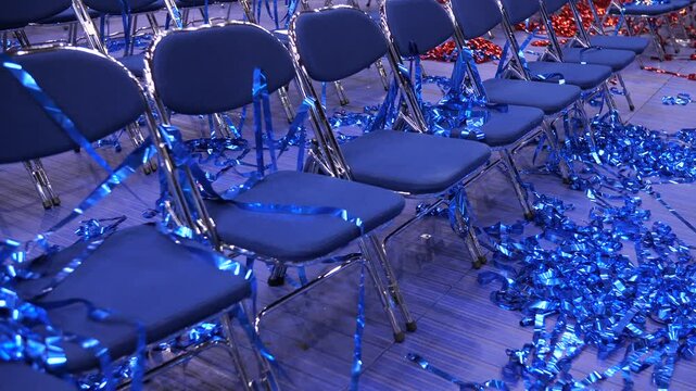 red and blue Confetti and tinsel on the floor. rows of empty blue chairs