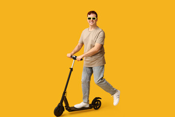 Young man riding modern electric kick scooter on yellow background