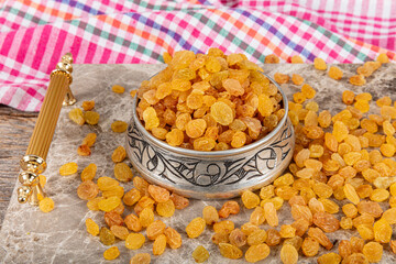 Sultani seedless raisins. Dried Sultani seedless raisins in a copper bowl served on a marble tray, raisins scattered around a copper bowl of raisins.