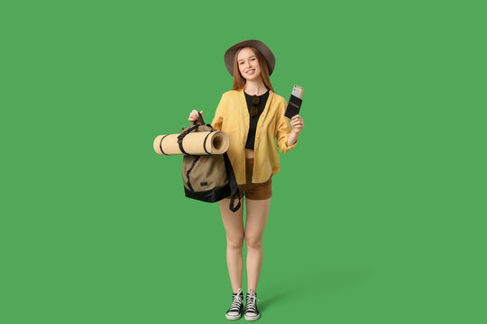 Smiling young woman with passport and backpack on green background. Travel concept